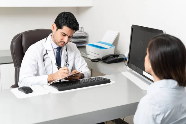 拉丁美洲男医生坐在诊所写字台边写药方 — 图库照片