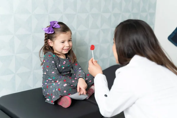 Mujer Pediatra Dando Piruleta Linda Niña Sentada Mesa Examen Oficina —  Fotos de Stock