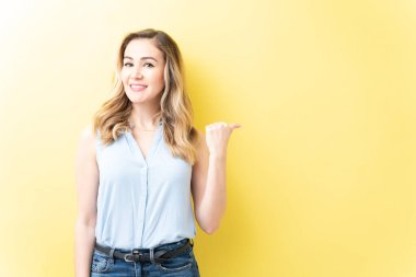 Sarı arka planda dikilirken sıradan hareketlerle gülümseyen çekici kadın.