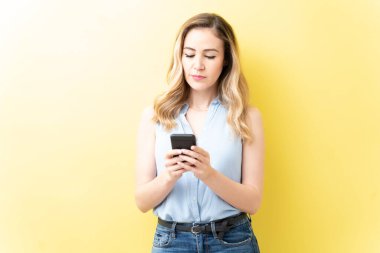 Güzel beyaz kadın sarı arka planda akıllı telefondan mesaj atıyor.