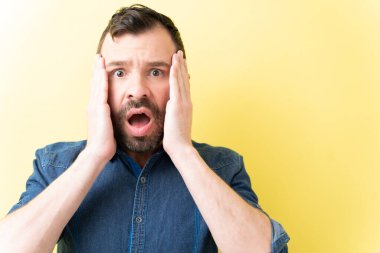 Sersemlemiş Latin bir adam, elleri sarı arka planda izole edilmiş.