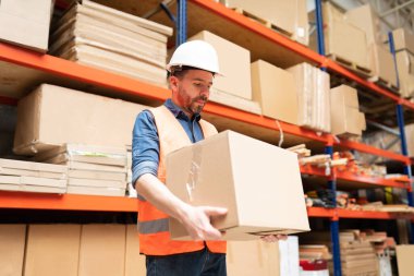 Depoda karton kutu taşıyan yakışıklı erkek işçinin düşük açılı görüntüsü.