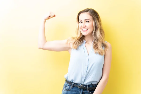Sorrindo Bela Mulher Flexionando Músculos Enquanto Contra Fundo Amarelo — Fotografia de Stock