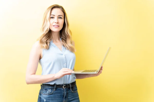 自信的成年女性站在黄色背景下使用笔记本电脑 — 图库照片