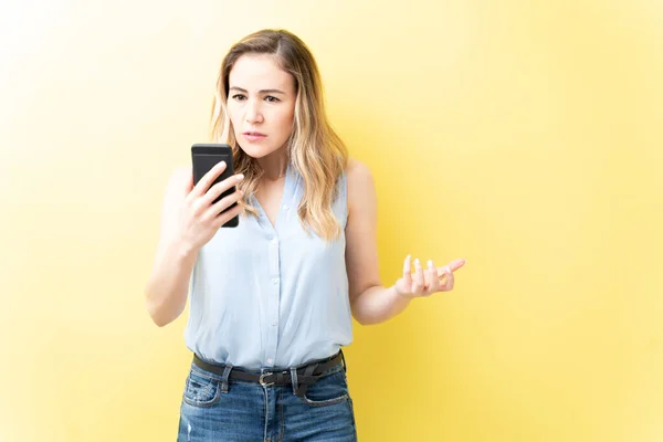 Gefrustreerde Volwassen Vrouw Zoek Naar Smartphone Tegen Een Gele Achtergrond — Stockfoto