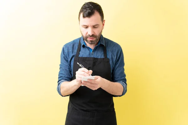 Latino Barista Masculino Escrevendo Ordem Diário Enquanto Contra Fundo Amarelo — Fotografia de Stock