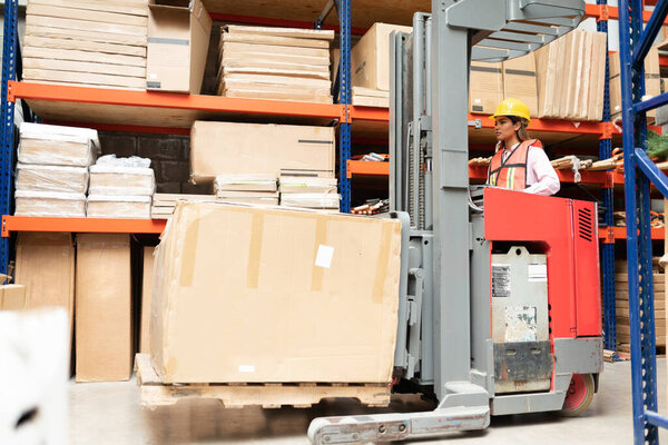 Hispanic female worker operating forklift by rack at factory