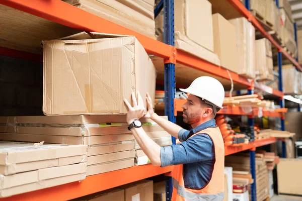 Side view of attractive male employee positioning cardboard box in rack at warehouse