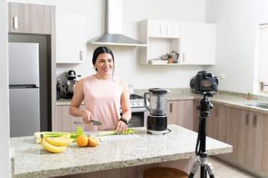 Gülümseyen, aktif beslenme uzmanı, kereviz keserken aynı zamanda mutfaktaki kameradan video bloğu yapıyor.