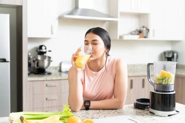 有魅力的活泼年轻女子靠着厨房柜台 闭目养神地坐在家里 一边喝着新鲜果汁 — 图库照片