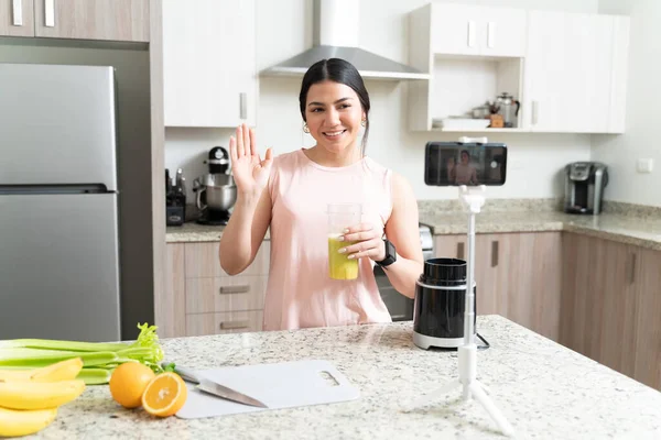 微笑美丽的年轻女性健康教练拿着果汁 一边在厨房里咒骂一边挥动着手机 — 图库照片
