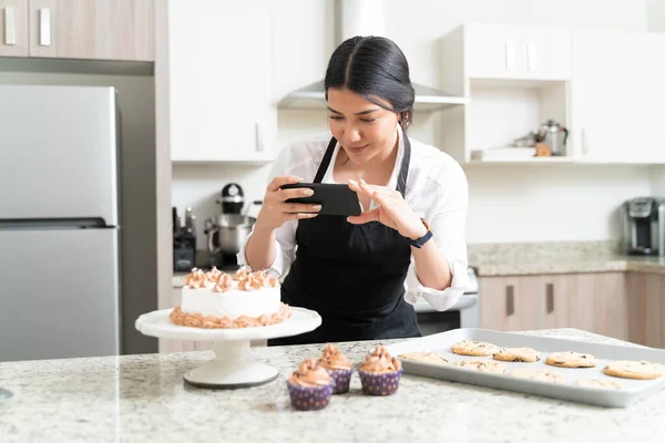 台所でソーシャルメディアのためのスマートフォンからケーキの写真を撮る美しい女性の食品写真家 — ストック写真