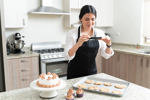 在厨房为社交媒体拍摄智能手机饼干的照片时 迷人的女性博主笑了 — 图库照片