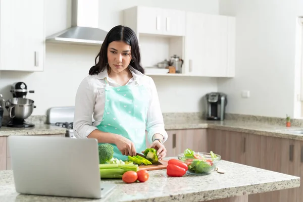 Attraktive Hausfrau Schneidet Paprika Und Lernt Gleichzeitig Online Vom Laptop — Stockfoto