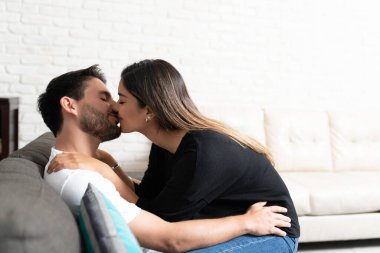 Romantik İspanyol çiftin evdeki oturma odasında öpüştüğü yan manzara.