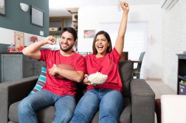 Neşeli erkek arkadaş ve kız arkadaş evde televizyonda Amerikan futbolu maçı izliyorlar.
