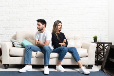 Kızgın erkek arkadaş ve kız arkadaş oturma odasında kollarını kavuşturup kanepede otururken gözlerini kaçırıyorlar.
