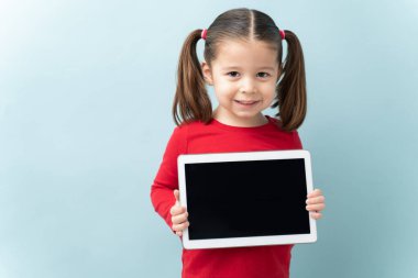 At kuyruklu mutlu küçük kız tablet bilgisayarın ekranını gösteriyor ve stüdyoda gülümsüyor.