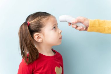 Stüdyoda küçük bir kızın ateşini ölçmek için termometre kullanan bir yetişkinin profil görüntüsü.