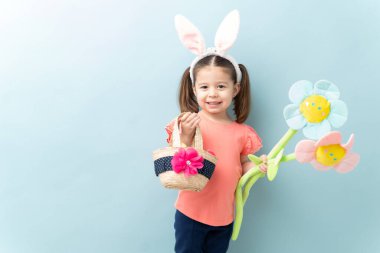 Güzel üç yaşında tavşan kulaklı, mavi arka planda fotokopi alanı olan Paskalya bayramını kutluyor.