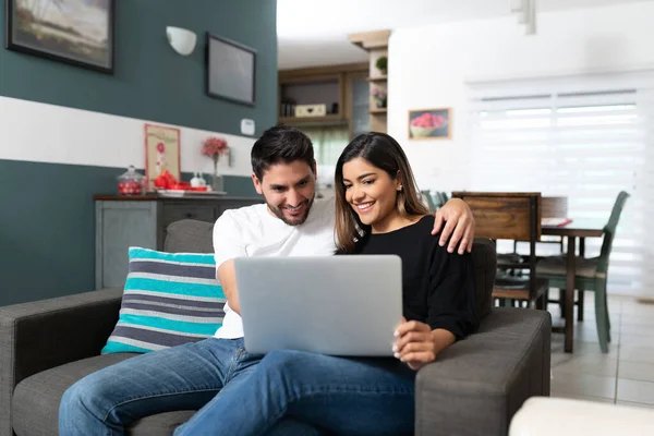 快乐的西班牙夫妇在家里客厅里坐在沙发上 一边用笔记本电脑 — 图库照片