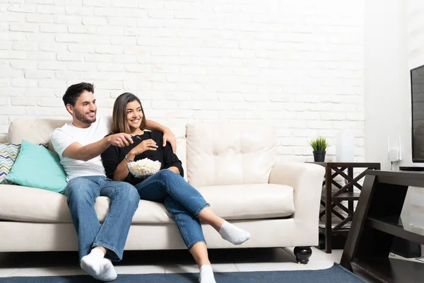 在家里客厅的沙发上一边看电视一边笑着的拉丁夫妻 — 图库照片