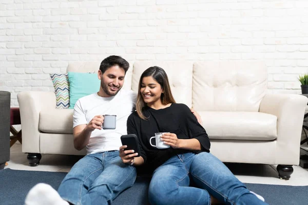 Pasangan Bahagia Hispanik Melihat Ponsel Sambil Minum Kopi Ruang Tamu — Stok Foto