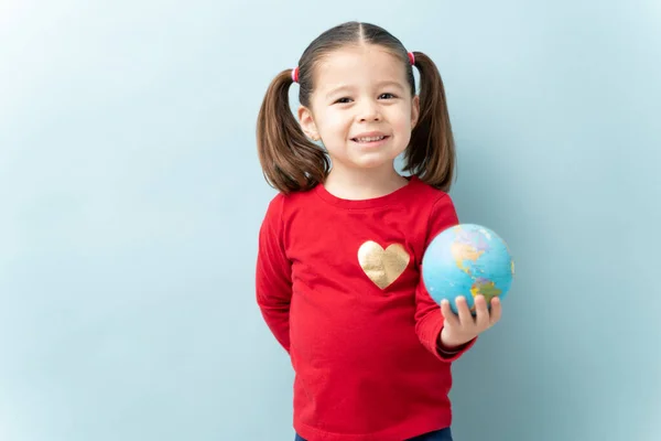 青い背景に笑顔で地球を保持ポニーテールとかなり小さな女の子の肖像画 — ストック写真