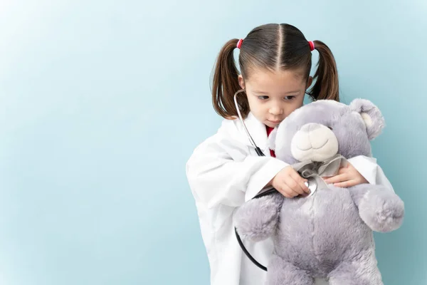 漂亮的小女孩 留着马尾辫 装扮成医生 用听诊器检查她的泰迪熊 — 图库照片