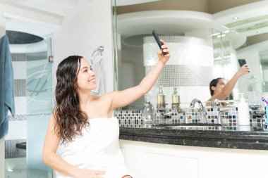 Banyoda duş aldıktan sonra akıllı telefonuyla özçekim yapan 30 'lu yaşlardaki hoş bir kadın.