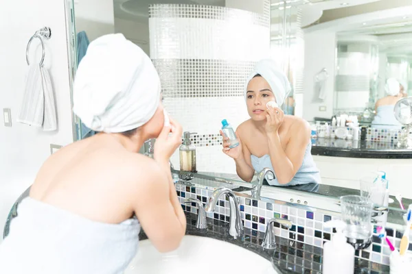 漂亮的女人裹在毛巾里 用棉垫在浴室镜子前卸妆 — 图库照片
