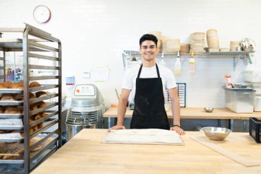 Önlük takan ve gülümseyerek fırında çalışan yakışıklı İspanyol bir adam.