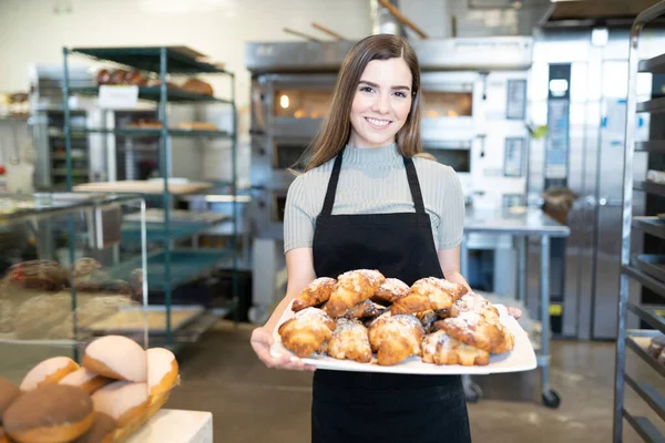 パン屋さんでおいしいペストリーがいっぱいのトレイを示すかわいい女性パン屋さんと笑顔 — ストック写真