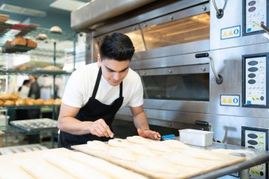 Erkek fırıncı fırına koymadan önce birkaç somun ekmek kesiyor.