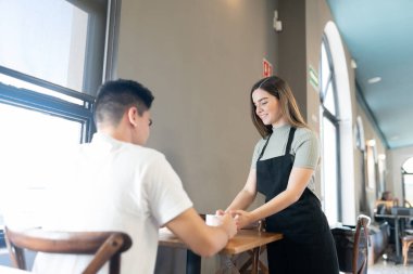 Kahve dükkanında çalışan güzel bir garson müşteriye kahve ve hamur işi getiriyor.
