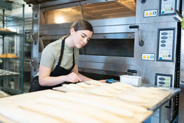 Fokuserad Kvinnlig Bagare Skära Upp Några Bröd Innan Bakar Dem — Stockfoto