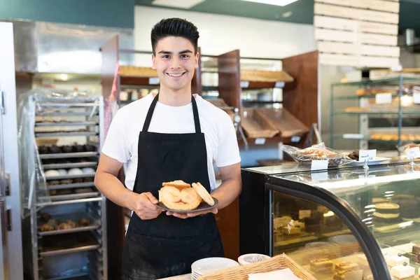 一个英俊的西班牙面包师在面包店里拿着盘子和他最爱吃的甜面包的画像 — 图库照片