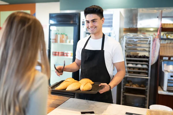 ハンサムなヒスパニック系の男パン屋で働くと笑顔で顧客にパンを販売 — ストック写真