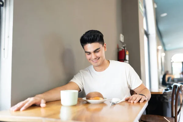 カフェでコーヒーと甘いパンを楽しんでいる魅力的な若い男と笑顔 — ストック写真