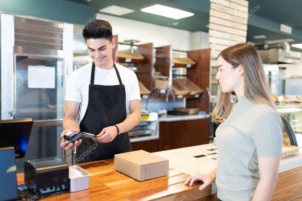 Handsome male worker using a bank terminal and credit card from a customer at checkout counter