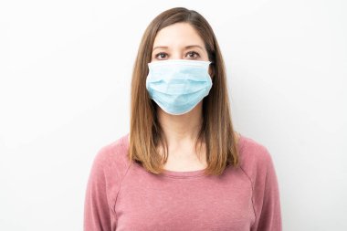 40 'lı yaşlarda cerrahi maske takan ve stüdyoda ciddi görünen bir kadının portresi.