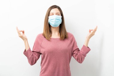 Cerrahi maskeli kadın stresle baş etmeye çalışıyor ve covid19 salgını sırasında meditasyon yapıyor.