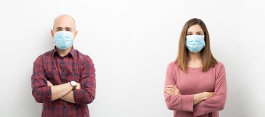 Stüdyo çekim konsepti, birbirinden uzak duran ve cerrahi maske takıp kollarını kavuşturarak sosyal mesafe çalışması yapan bir çift.