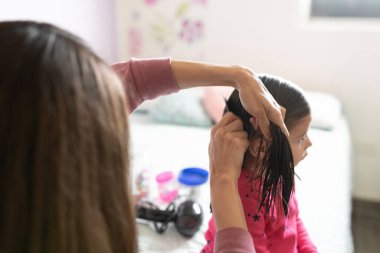 Evde küçük bir kızın saçını tarayan bir annenin bakış açısı yakından görülüyor.