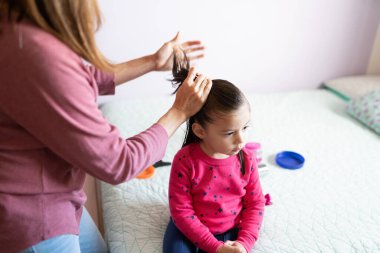 Küçük kızına at kuyruğu yapan bir annenin yüksek açılı görüntüsü.