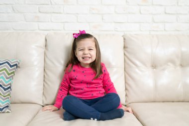 Evdeki bir kanepede oturan ve mutlu görünen küçük beyaz bir çocuk.