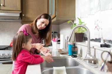 Güzel beyaz anne kızına mutfak lavabosunda ellerini nasıl yıkayacağını gösteriyor.