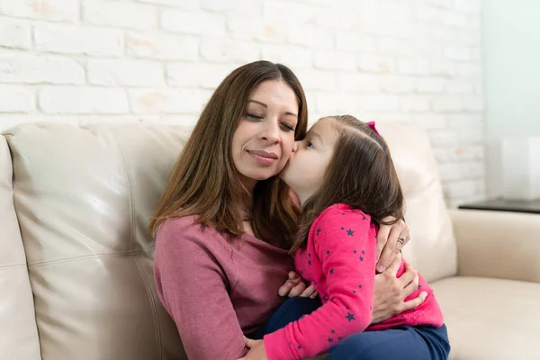 一个母亲在家里客厅里放松的时候 被女儿吻在脸颊上的画像 — 图库照片