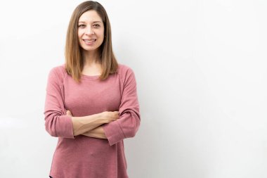 Stüdyoda kollarını kavuşturup gülümseyen güzel beyaz bir kadın.