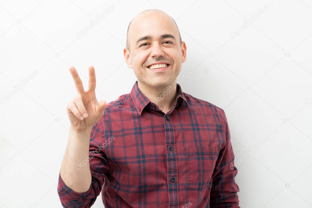 Portrait of an attractive bald man making a peace and love sign with his hand and smiling